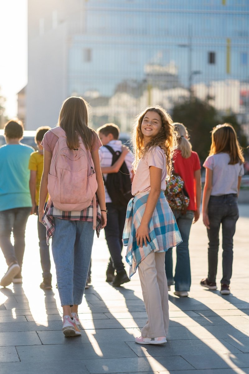 Rear view of happy teenagers with backpacks walking in the city